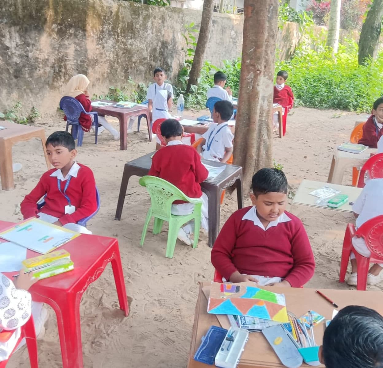Students sitting on grass, drawing and painting outdoors with easels.